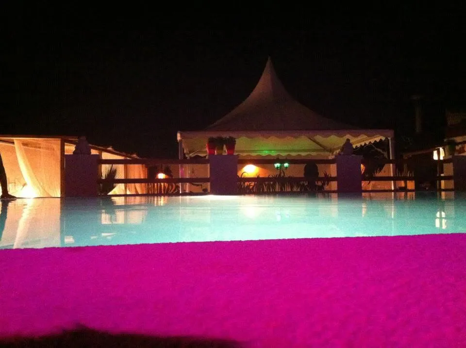 Lámina de agua de la piscina de noche con el borde fucsia y la carpa iluminada